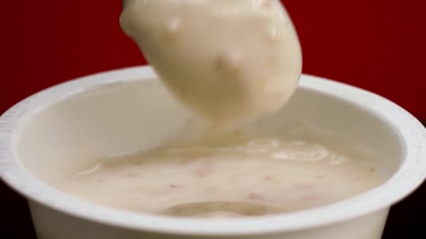 Comer yogur con cereales de un frasco de plástico con una cuchara. Imágenes de archivo. Primer plano de yogur griego aislado sobre fondo rojo, desayuno saludable o merienda. — Vídeo de stock