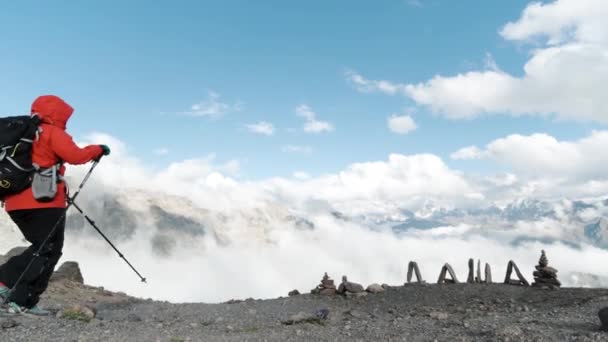 Groep wandelaars gekleed in warme skipakken wandelen naar rand klif met witte pluizige bergen. Een knip. Vrouwelijke naam gemaakt van stenen en reizigers mannen en vrouwen lopen op een stenig vlak oppervlak met ski — Stockvideo