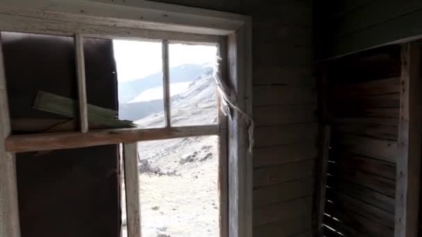 Vista a través de las ventanas dentro de una casa abandonada de madera. Clip. Antiguo edificio de madera en ruinas y una pendiente de la colina exterior. — Vídeos de Stock