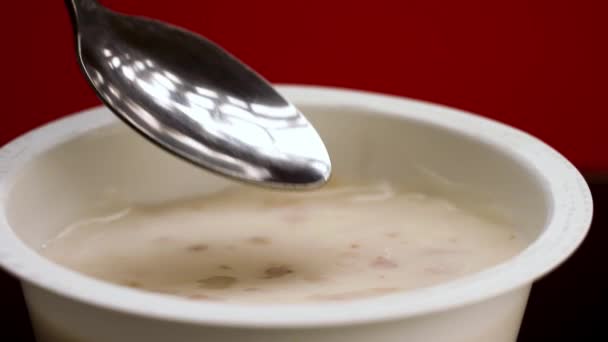 Jedzenie jogurtu ze zbożem z plastikowego słoika z łyżką. Materiał filmowy. Zbliżenie greckiego jogurtu izolowanego na czerwonym tle, zdrowe śniadanie lub przekąska. — Wideo stockowe