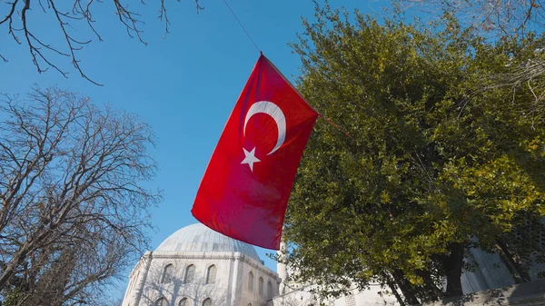 Turkish flag on background of mosque. Action. Turkish flag is flying in square near mosque. Travel around capital of Turkey - Istanbul with Islamic sights and mosques. Flag of Turkey