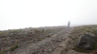 Sisli rüzgârlı bir havada, kayalık bir dağ yamacında yürüyen bir yürüyüşçü. Şarjör. Bir tepeden inen yalnız bir turist.