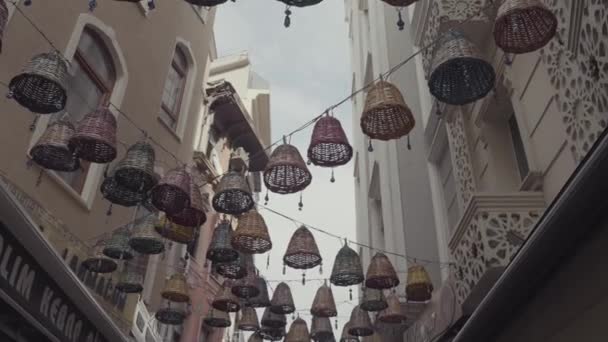 Bottom view of beautiful wicker baskets with nazar amulets hanging in the city streets between buildings. Action. Narrow street details, Istanbul, Turkey. — Stock Video