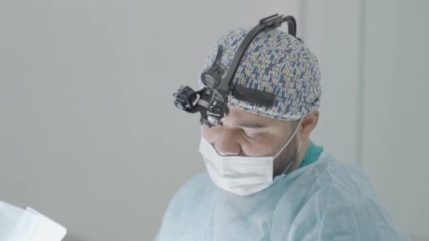 Surgeon in binoculars. Action. Young professional surgeon is preparing for operation. Surgeon prepares for operation, washes hands and prepares place — Stock Video