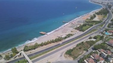 Kıyı manzarası ve kumlu gök mavisi okyanus. Şarjör. Alanya, Türkiye, şehir binaları üzerinde ve uzun düz yolda sürüş arabalarıyla uçuyor.