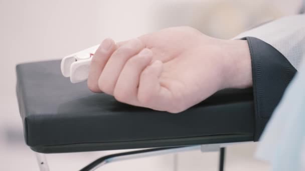 Close-up van een menselijke hand met een sensor aangesloten. Actie. Verdoofde patiënt met een hartslag aan de vinger tijdens de operatie. — Stockvideo