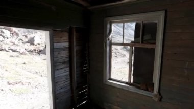 Terk edilmiş ahşap bir evin penceresinden bak. Şarjör. Eski harabe ahşap bina ve dışarıda bir tepe var..
