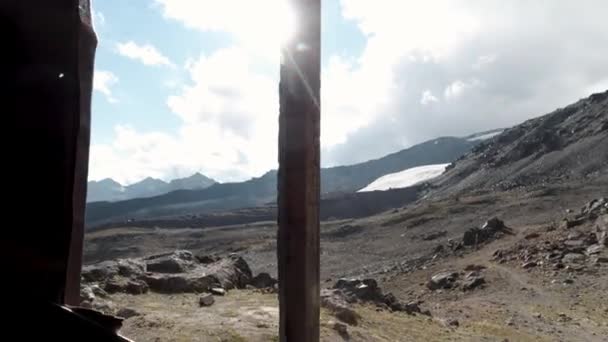 Vista a través de la ventana arruinada en el paisaje montañoso. Clip. Mirando a través de una vieja ventana de madera sin vidrio en la hermosa pendiente de la montaña y el cielo azul. — Vídeos de Stock