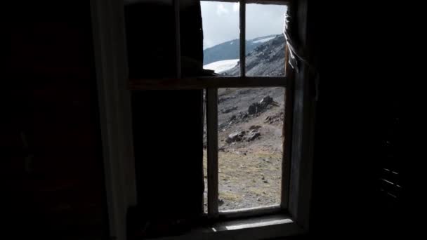 Vue à travers fenêtre en ruine sur paysage montagneux. Clip. Vue à travers une vieille fenêtre en bois sans verre sur une belle pente de montagne et un ciel bleu. — Video