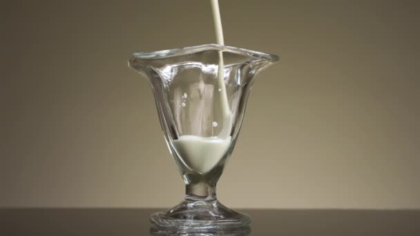 Tutup dari menuangkan susu atau yogurt ke dalam gelas transparan yang terisolasi pada latar belakang dinding beige. Rekaman saham. Konsep kalsium dan sarapan sehat. — Stok Video