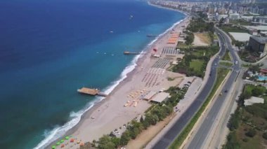 Kıyı manzarası ve kumlu gök mavisi okyanus. Şarjör. Alanya, Türkiye, şehir binaları üzerinde ve uzun düz yolda sürüş arabalarıyla uçuyor.