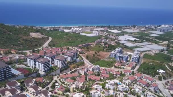 Aerial panoramic view of a coastal town and blue calm sea. Clip. Summer city on a sunny day with many residential houses and green trees. — Stock Video