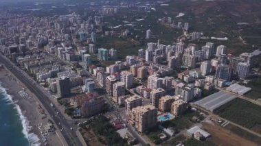 Kıyı şehri manzarası, yaz kasabası manzarası, tatil kavramı. Şarjör. Deniz kenarındaki yeşil bitki örtüsüyle modern güney şehri üzerinde uçuyor..