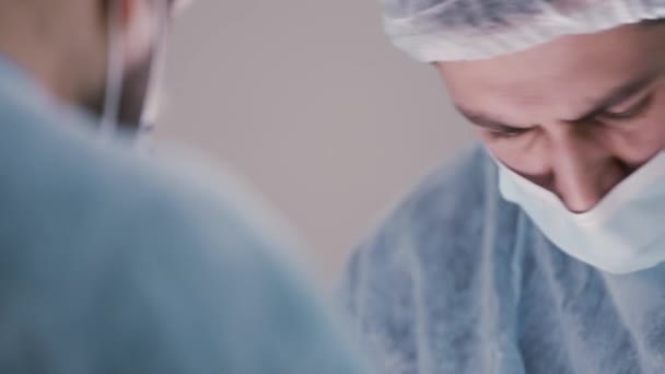 얼굴에 마스크를 쓰고 보호 모자를 쓴 젊은 남성 의사나 보조의 모습. 행동. 의사가 수술중에 평온 한 감정을 가지고 아래를 내려다보는 것, 의학 개념. — 비디오