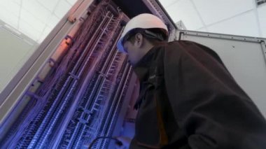 Elektrik tesisatçısı elektrik kutusunda çalışıyor, bağlantıları tamir ediyor. Başla. Elektrik santralinde koruyucu üniformalı ve miğferli bir elektrikçinin alt görüntüsü..