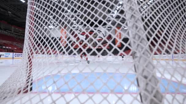 Eishockeyspieler trainiert allein auf Eisbahn. Handeln. Blick durch das Gitter des Tores an der Eisbahn. Eishockeyspieler trainiert allein, um auf der Eisbahn den Puck zu treffen. Zeitlupe — Stockvideo