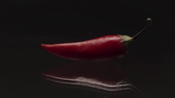 黒の背景にガラスの透明な表面に横たわるスパイシーな赤唐辛子のクローズアップ。ストック映像だ。新鮮な野菜、食べ物や料理の概念. — ストック動画