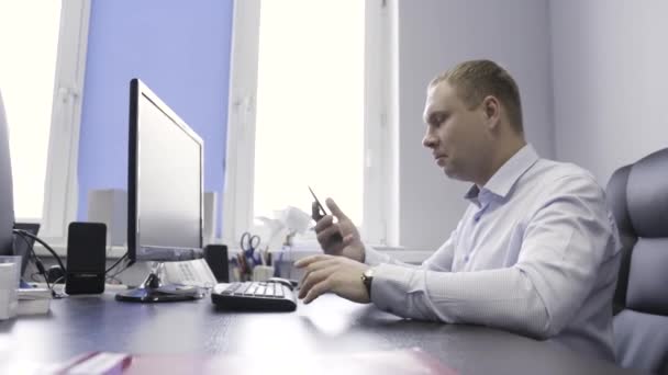ビジネスマンは、コンピュータの画面の前で彼のオフィスで働いている。行動だ。携帯電話で仕事の話をしているシャツの男の側面図. — ストック動画