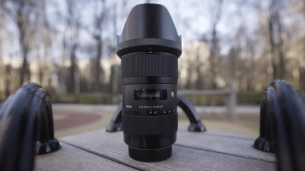 Close-up van een nieuwe professionele zwarte fotocamera lens liggend op houten planken oppervlak op wazig natuurlijke achtergrond. Actie. Concept van kunst en fototechnologieën. — Stockvideo