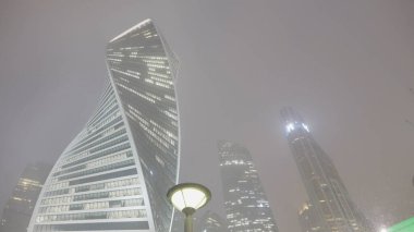 Kar yağışı altında modern gökdelenler. Başla. Geceleri kar yağarken parlayan gökdelenleri olan bir iş merkezi. Gece karlı bulutlu gökyüzünün arka planında güzel bir iş var.