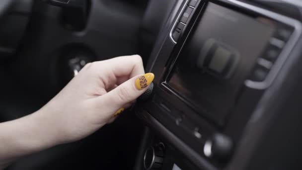 El conductor ajusta el volumen de una radio dentro de un coche. Acción. El primer plano de la mano femenina con la manicura amarilla que gira el control del volumen, los detalles del interior del automóvil. — Vídeos de Stock