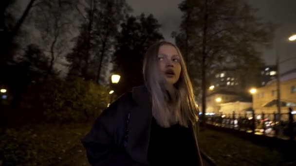 Испуганная девушка, бегающая одна в парке ночью. Начали. Блондинка боится, что кто-то последует за ней, оглянется вокруг. — стоковое видео