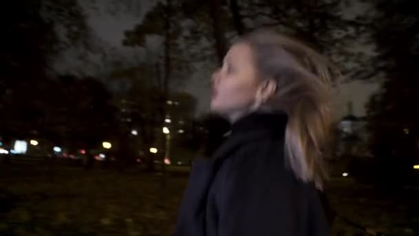Испуганная девушка, бегающая одна в парке ночью. Начали. Блондинка боится, что кто-то последует за ней, оглянется вокруг. — стоковое видео