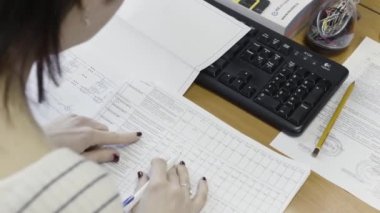 Ofisteki masasında belgelerle çalışan bir kadın muhasebecinin omzunun üstünden bak. Başla. Kadın eli kağıtlı ve bilgisayar klavyesinin yanındaki kalemi kapat..