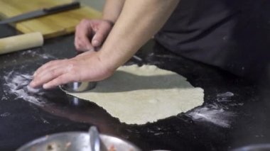 Aşçı hamuru kesiyor. - Sanat. Mantı için hamur hazırlayan profesyonel şefin yakın çekimi. Geleneksel hamur işleri için yuvarlak hamur parçaları kesiyorum.