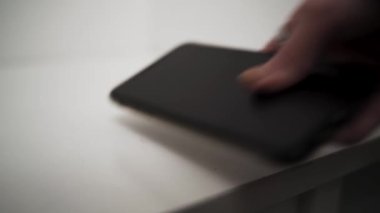 Erkek eli siyah cep telefonunu beyaz arka planda izole bir masaya koyar. Başla. Erkek eli kapalı, akıllı telefonu masaya koyuyor..