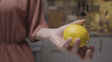 Elinde taze limon tutan kahverengi elbiseli zayıf bir kadının fotoğrafını çek. Başla. Evde mutfakta yemek pişirme kavramı..