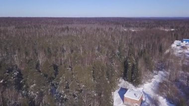 Kış ormanının arka planındaki evin en üst manzarası. Şarjör. Güneşli kış gününde ormanın ortasında bir kır evi. Sonsuz çam ormanının yanındaki ev ufka ulaşıyor.