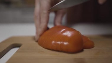 Salata için biber kesen çelik bıçaklı kadın eller, sağlıklı vejetaryen yemeği kavramı. Başla. Mutfak masasındaki taze biberin kapağını bir ev hanımı keser..