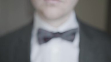 Papyonu ayarlayan beyefendinin yakın çekimi. Başla. Çekici adam destansı bir şekilde papyonu takım elbiseye ayarlıyor. Kibarca ve cesurca papyonu düzeltir.