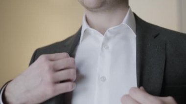 Takım elbise montunu ayarlayan beyefendinin yakın çekimi. Başla. Çekici adam kutlamadan önce smokini ayarlar. Beyefendi ceketini düzeltir ve düğmelerini ilikler.