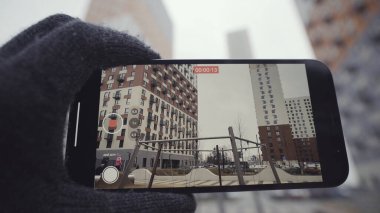 Sıcak eldiven giymiş bir erkeğin, çocukların arka planlarını ve çok katlı binaları videoya çekerken fotoğrafını çek. Başla. Akıllı telefon kamera kalitesinin gösterimi.