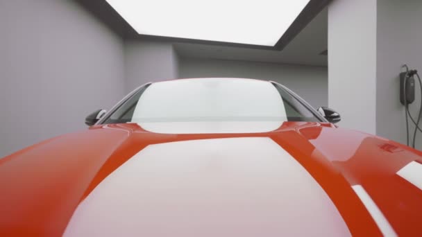 Close-up da vista frontal de um carro esporte de luxo vermelho estacionado na garagem. Acção. Pára-brisas e capuz de carro sob o holofote brilhante. — Vídeo de Stock