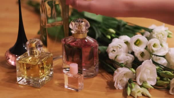 Маленькі пляшки з парфумами і квітами на дерев'яному столі. Поняття. Крупним планом жінка вибирає аромат і бере одну рукою . — стокове відео