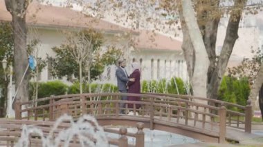 Briç parkında romantik bir çift. Başla. Doğulu güzel bir çift parktaki ahşap köprüde duruyor. Yetişkin bir çift, güzel manzaranın arka planında romantik bir şekilde durur.