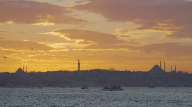 Günbatımı arkaplanlı güzel İstanbul manzarası. Başla. Günbatımının arka planında camilerin siluetleri olan karanlık sahil. İstanbul açıklarında gün batımında gemiler ve martılarla dolu bir deniz.