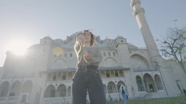 美しい女性の寺院の背景にポーズ。行動だ。晴れた日には幸せな女性がモスクの外で踊る。美しい女性が太陽の光を背景にモスクの近くを旋回 — ストック動画