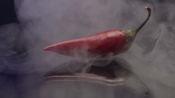 Крупный план красного острого перца чили, лежащего на зеркальной поверхности с пятнами дыма. Запись. Пряный свежий овощ и облака белого дыма. — стоковое видео