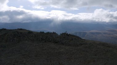 Kamera yeşil yamaç boyunca bir dağın tepesine doğru hareket ediyor. Şarjör. Bulutlu gökyüzü arkaplanındaki yeşil tepenin hava görüntüsü.