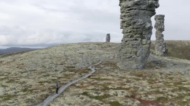 Rotsformaties op de top van een berg. Een knip. Luchtfoto van een toerist die staat en kijkt naar een gigantische stenen pilaren met bewolkte lucht en beboste heuvels op de achtergrond. — Stockvideo