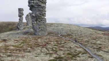 Bulutlu arka planda, tepenin üstünde doğal taş heykeller. Şarjör. Dev taş sütunların yanında çok küçük görünen bir adam, Manpupuner, Comi Republic, Rusya.