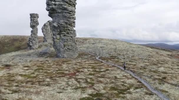 Natuurstenen sculpturen op een heuveltop op bewolkte hemelse achtergrond. Een knip. Een man die er heel klein uitziet in de buurt van gigantische stenen pilaren, Manpupuner, Comi republiek, Rusland. — Stockvideo