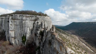Dağların arka planındaki kayalık uçurumun en üst manzarası. Vuruldu. Tepe bölgesindeki görkemli kayalık kayalıklarla güzel bir manzara. Kayalar, kayalıklar, tepeler ve ovalar bir arazide