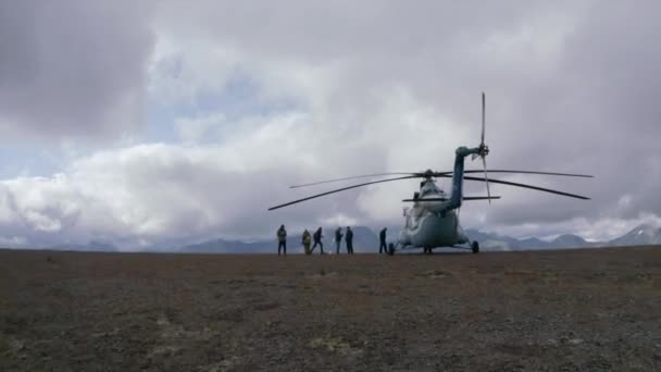 贅沢と高価な観光の概念:山の上にヘリコプターの近くの人々のグループ。クリップ。素晴らしい野生の緑の丘と曇った空の美しさを探索するハイカー. — ストック動画