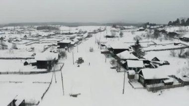 Kırsal kesimde karla kaplı çatıları olan küçük bir kasabanın üzerinde uçmak. Şarjör. Soğuk bir kış gününde küçük sakin bir köyün hava manzarası, Sibirya, Rusya.