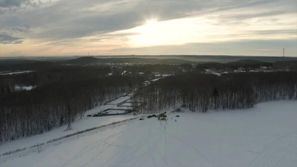 Veduta aerea del tramonto sul campo innevato con tracce di motoslitta e bosco. Clip. Foresta e colline ghiacciate sullo sfondo. — Foto Stock